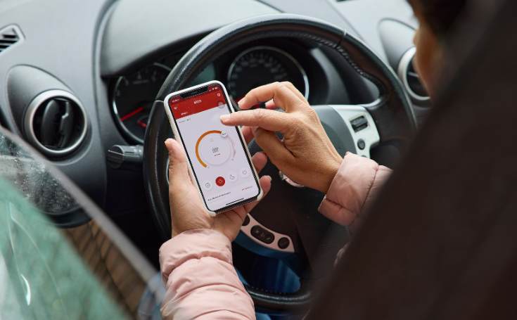 Handy mit geöffneter REMOCON NET-App zur Fernsteuerung der Heizung, im Auto gehalten