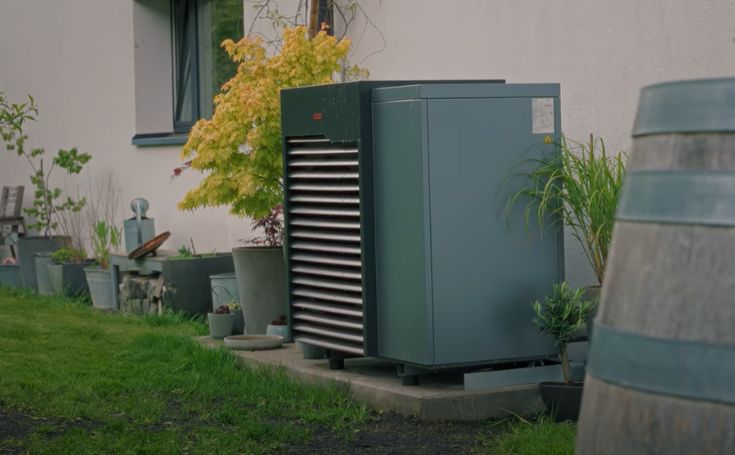 Pompe à chaleur installée à l’extérieur d’une maison, entourée de plantes et de pots de fleurs dans un jardin.